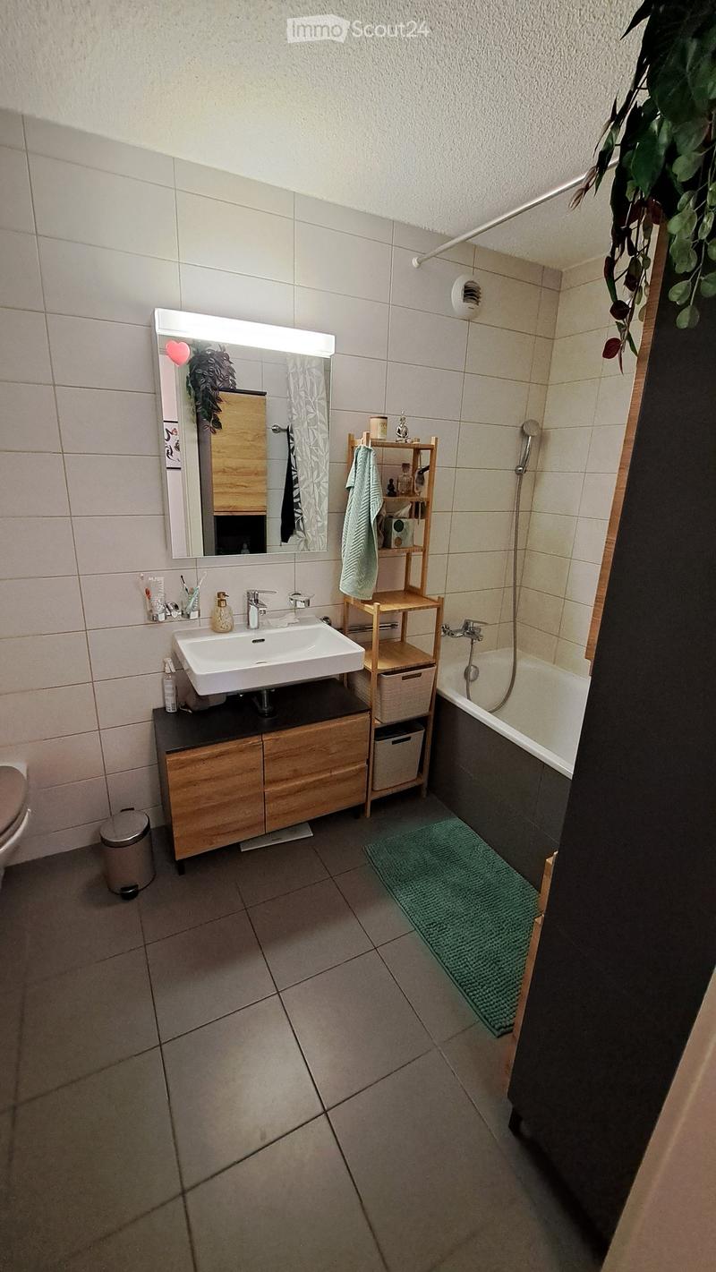 Modern bathroom with a white sink, wooden cabinet, mirror, towel rack, bathtub, and a green bath mat.