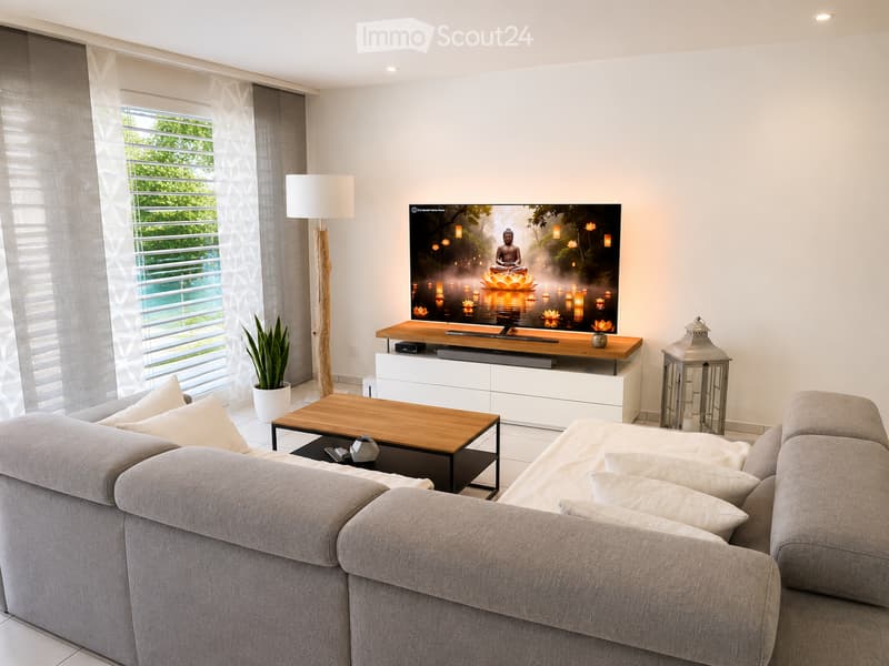 Modern living room with a grey sectional sofa, wooden coffee table, TV stand with a large flat-screen TV, floor lamp, and a potted plant near the window.