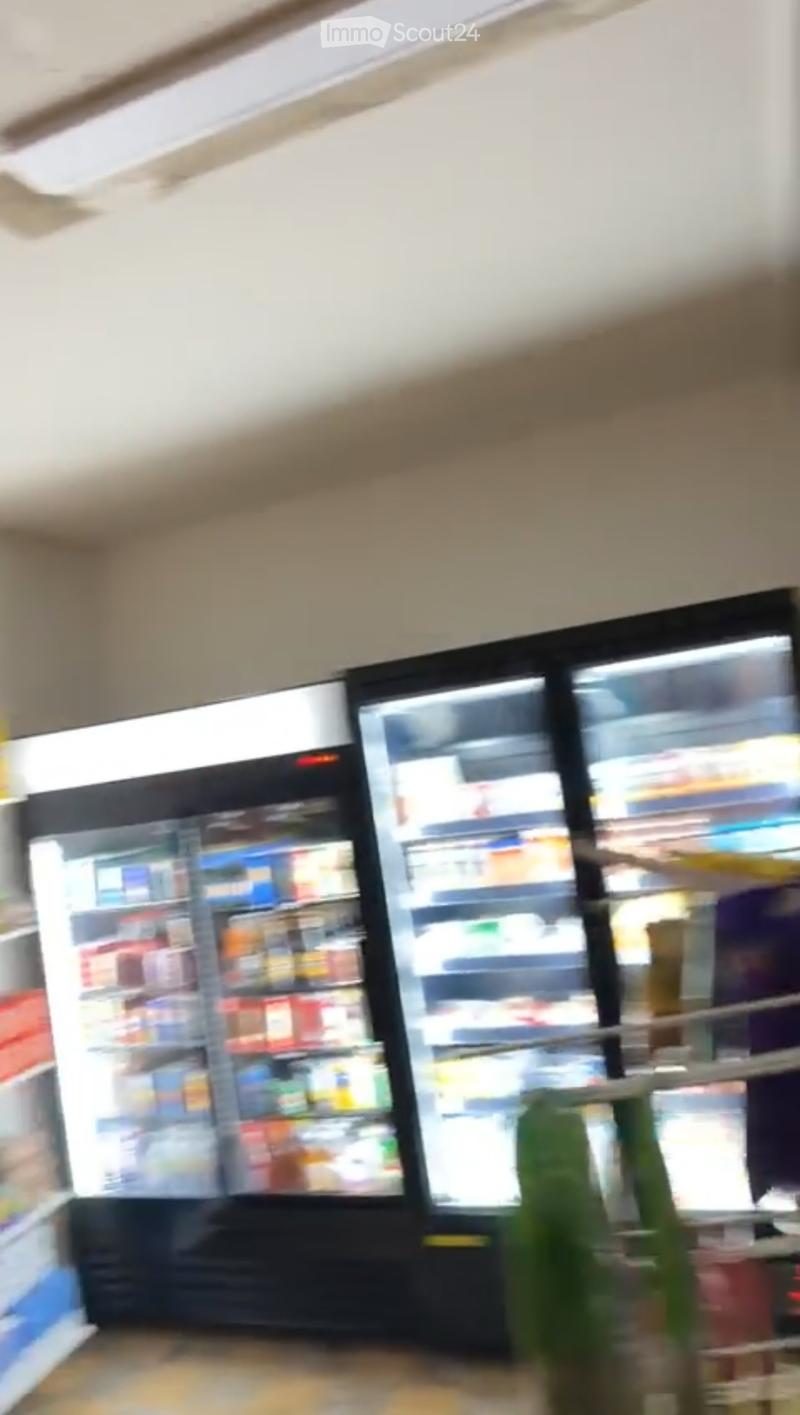 A small convenience store or mini-market interior with a large refrigerator unit displaying various beverages and snacks.