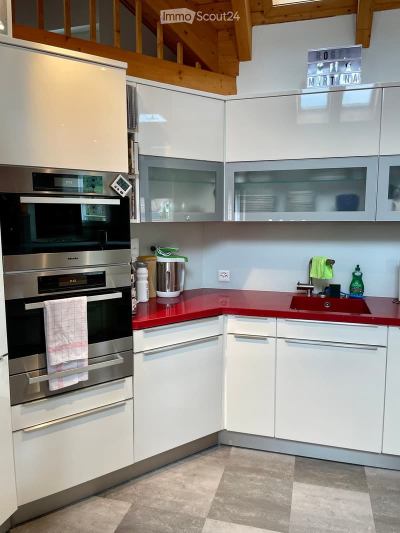 Modern kitchen with white cabinets, red countertops, stainless steel appliances, and a sink with a faucet.