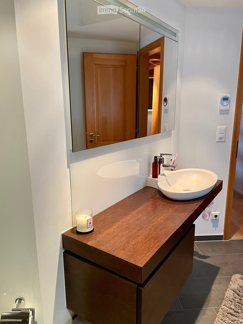Modern bathroom with a wooden vanity, double sink, large mirror, and various toiletries.