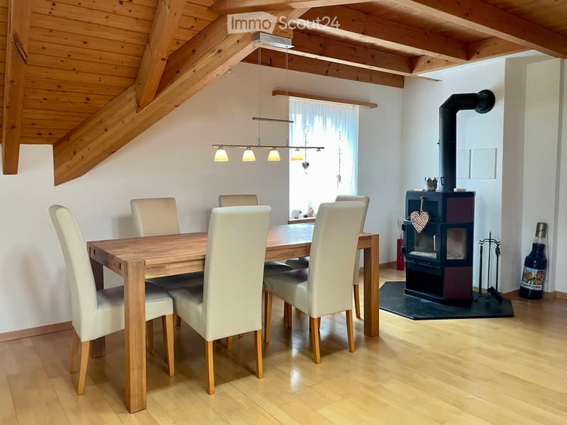 Dining room with wooden table, white chairs, wood stove, and pendant lights.