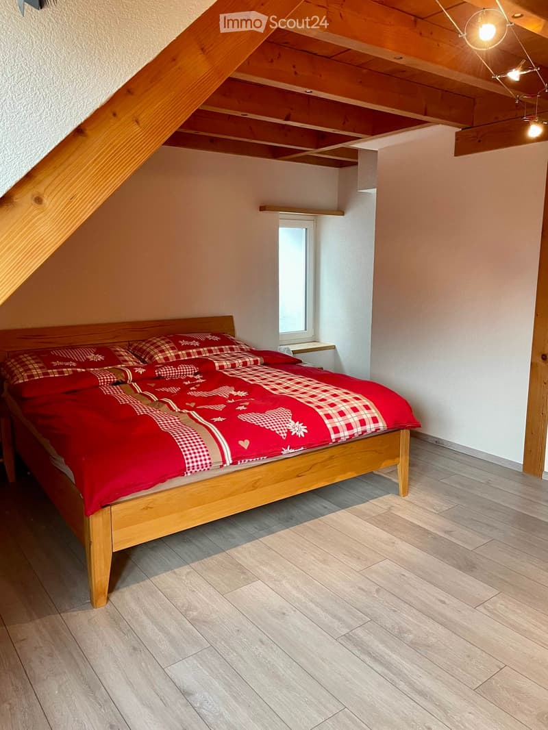 Cozy attic bedroom with wooden slanted ceilings, a single wooden bed with red and white checkered bedding, and a small nightstand next to a window.