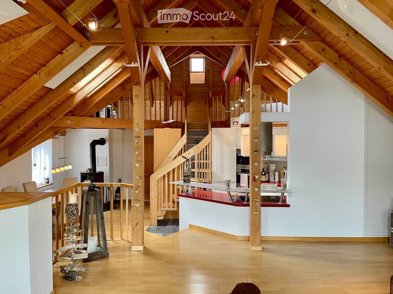 Open-plan living and dining area with exposed wooden beams, a staircase leading to an upper level, a modern kitchen island, and a cozy seating area with a fireplace.
