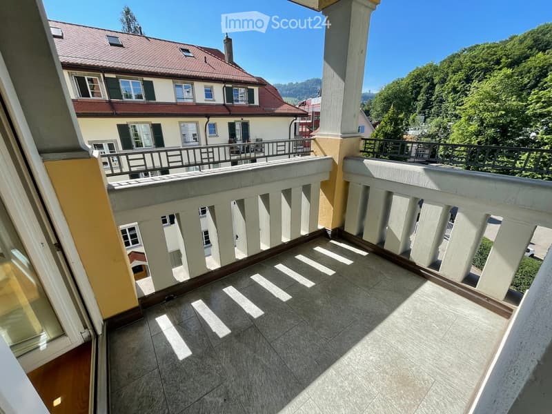 Balcony with tiled floor, white balustrade, overlooking a residential building and green landscape.
