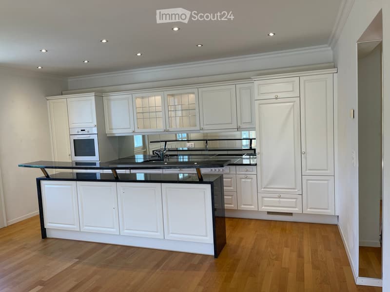 Modern kitchen with white cabinets, black countertop, and wooden flooring.