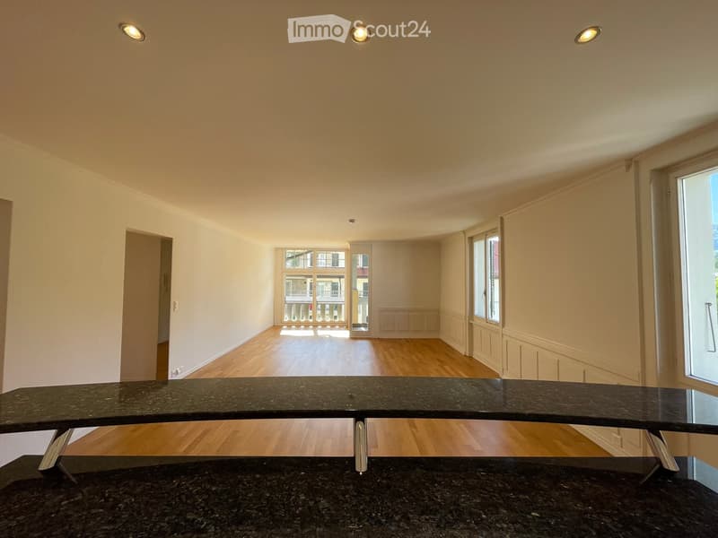 Empty room with wooden flooring, white walls, and large windows allowing natural light. No furniture or furnishings are present.