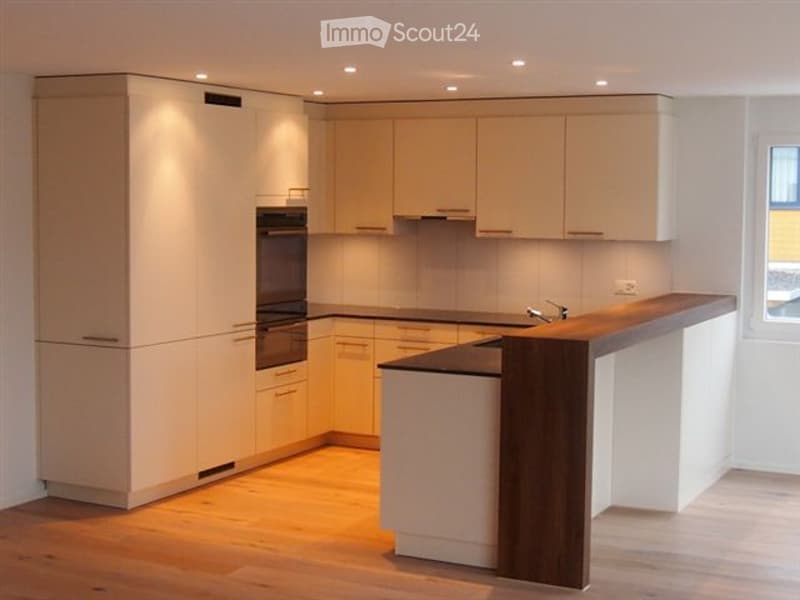 Modern kitchen with white cabinetry, wooden flooring, and a central island with a dark wood countertop.
