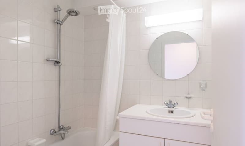 Modern bathroom with white tiles, a bathtub, a sink with a mirror, and a shower head.