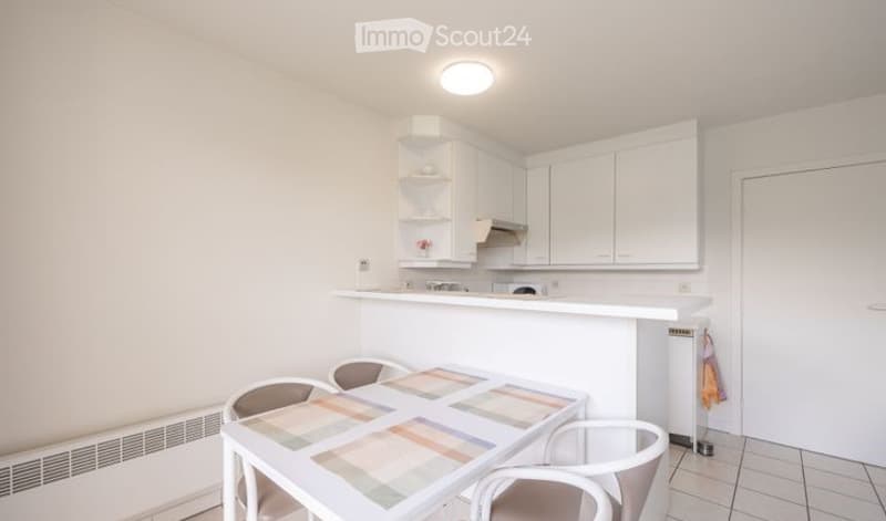 Bright, modern kitchen and dining area with white cabinets, a countertop, a small dining table with chairs, and a refrigerator.