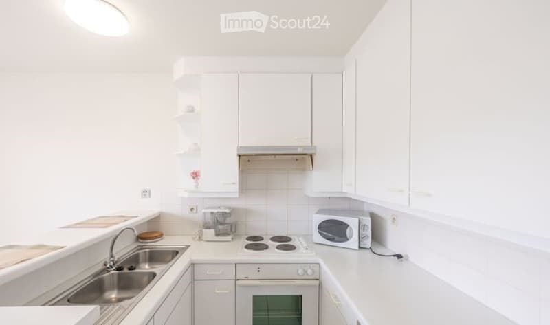 Modern kitchen with white cabinets, stainless steel sink, electric stove, microwave, and coffee maker. Features built-in storage and sleek design.