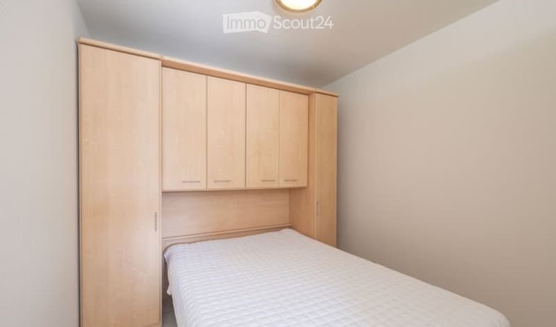 Minimalist bedroom with a single bed, built-in wooden wardrobe, and neutral-colored walls.