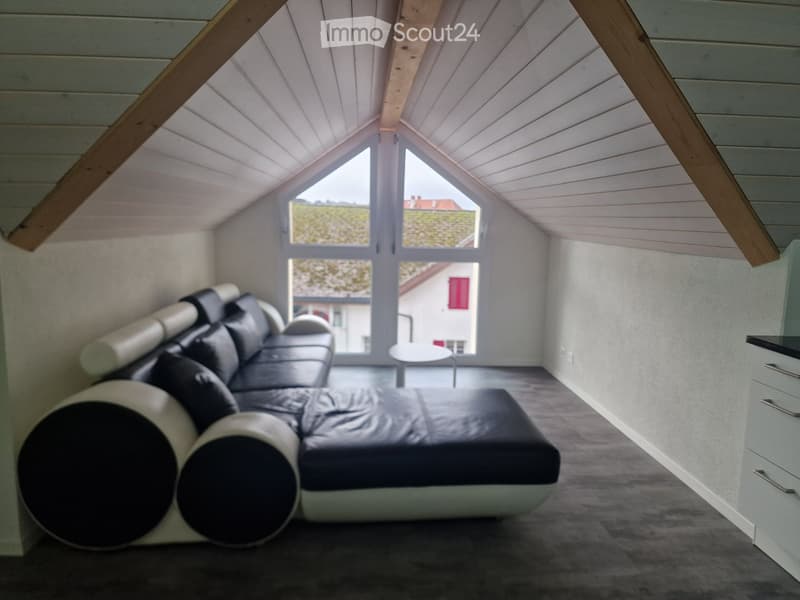 Modern loft-style room with a black leather sofa, white cylindrical armrests, a small white round table, and large windows offering a view of the outside.