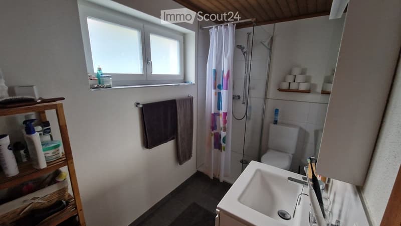 Bathroom with white tiles, white sink, shower, toilet, towel rack, window, wooden shelf with toiletries