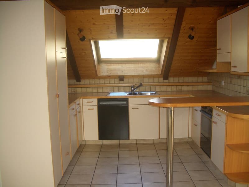 Bright kitchen with wooden cabinets, tiled floor, sink, dishwasher, and a small table.