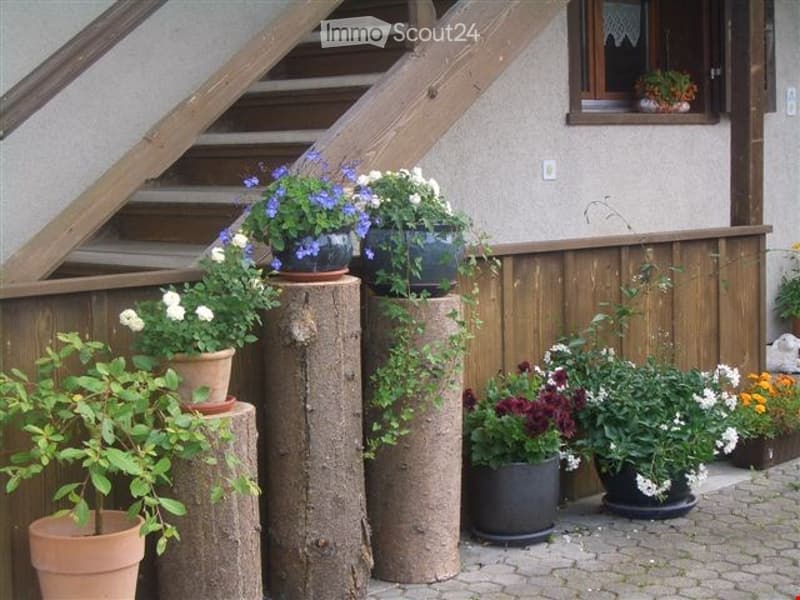 Garden area with potted plants on wooden stumps and a wooden fence, with a house staircase and window in the background.