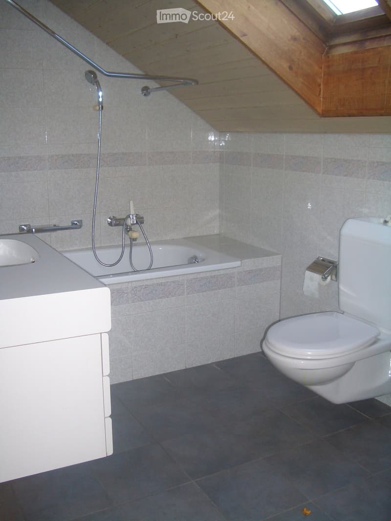 Bathroom with a toilet, bathtub, sink, and faucet. The walls are tiled, and the floor is covered with dark tiles.