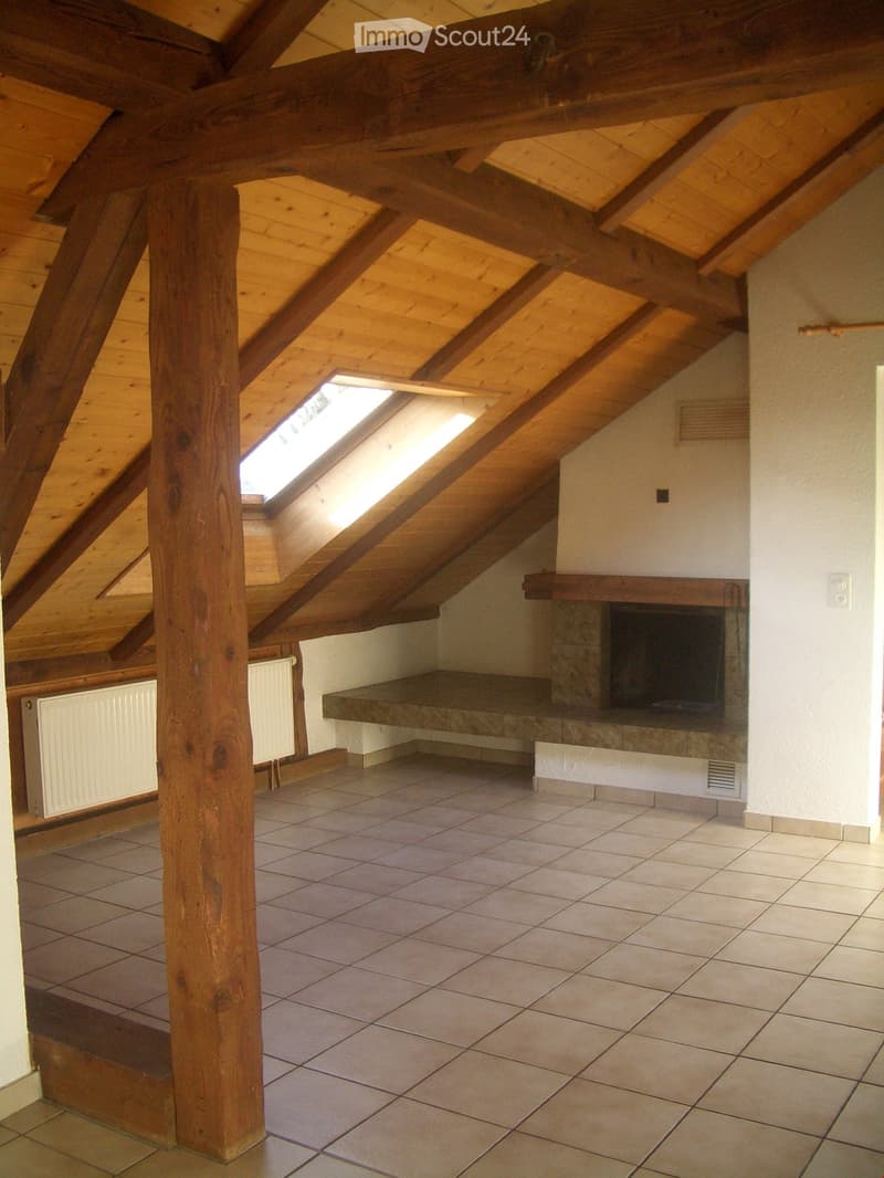 An attic space with exposed wooden beams, tiled floor, and a fireplace with a stone surround. Skylights provide natural light.