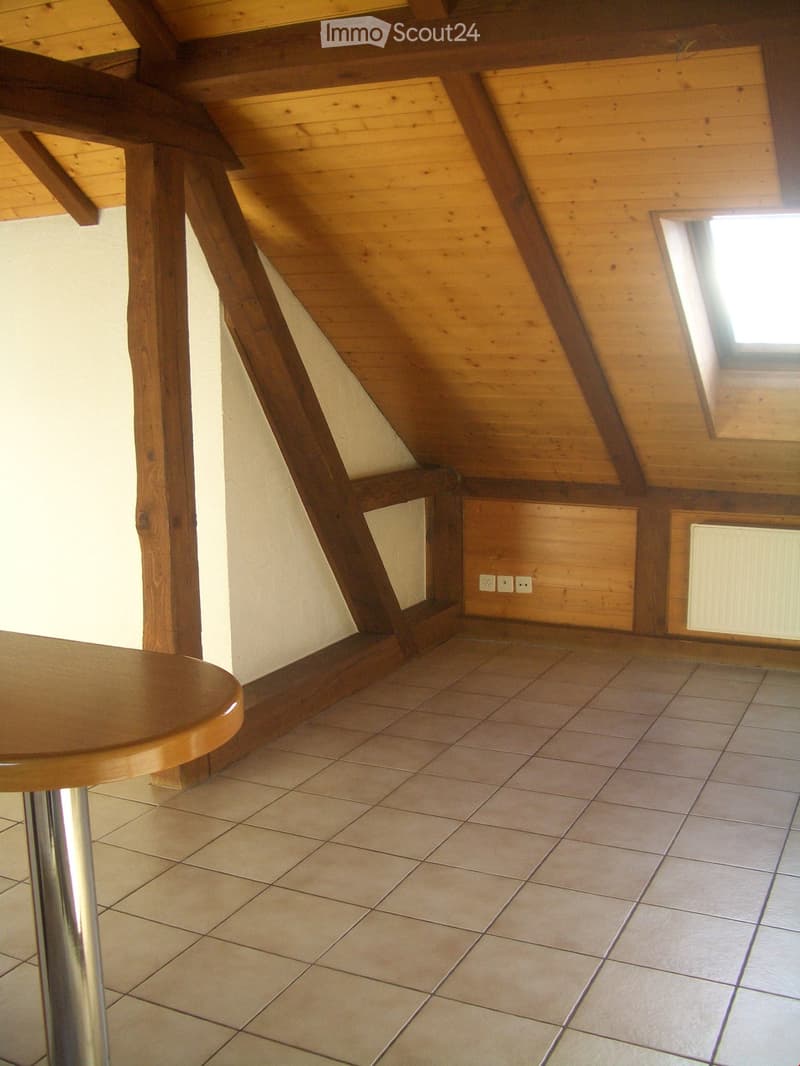 Loft-style room with wooden beams, tiled floor, and a small round table with a metal base.