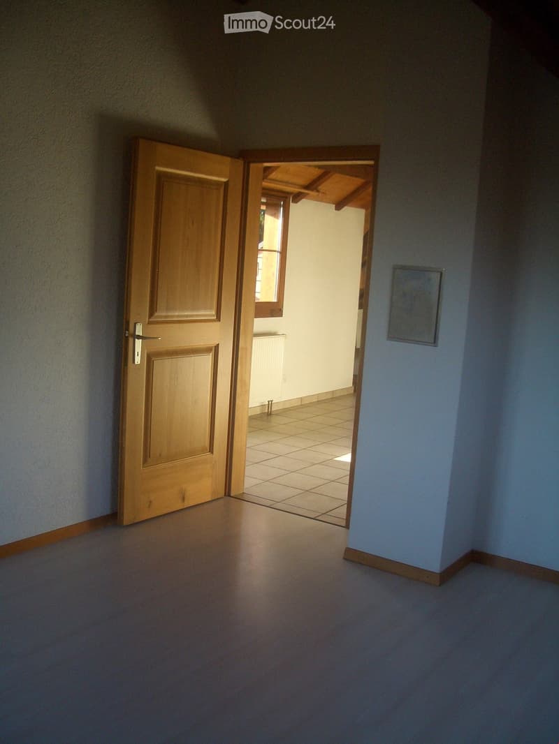 Empty hallway with wooden doors, light blue walls, and a tiled room visible through an open doorway.
