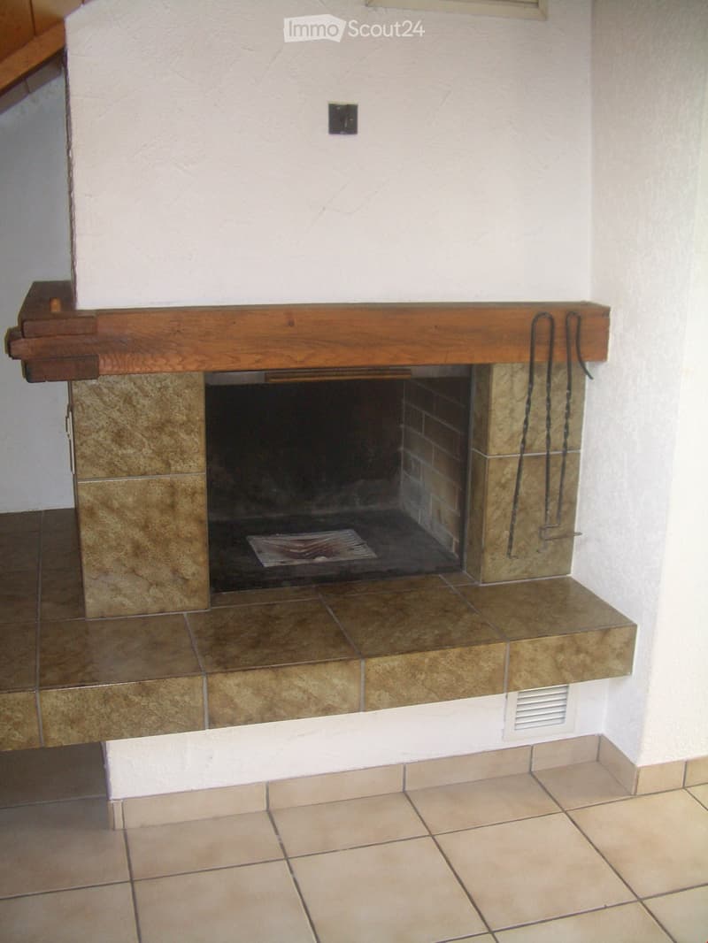 A fireplace with a wooden mantel and tiled surround, set into a tiled floor area.