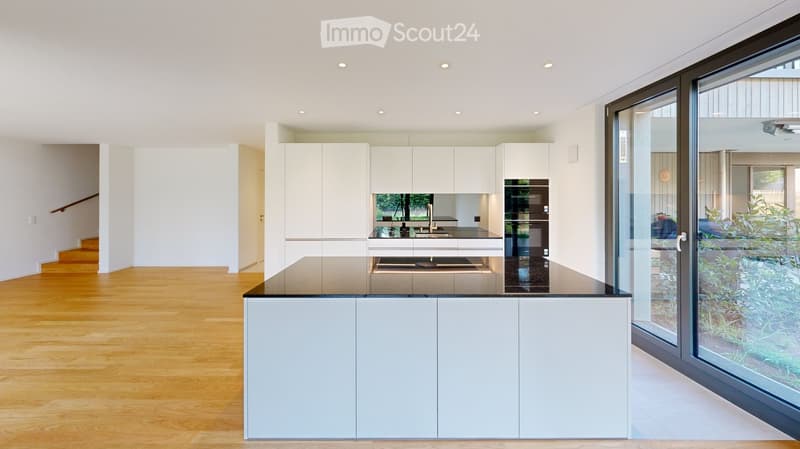 Modern kitchen with white cabinets, black countertop, and a large window overlooking a garden area.
