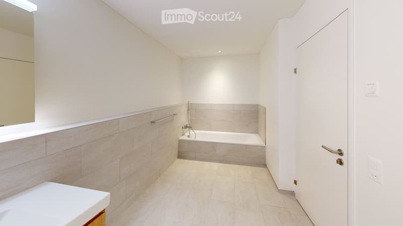 Modern bathroom with a bathtub, sink, and mirror. Light-colored tiles and a sleek design.
