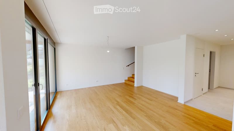 Empty room with light wooden flooring, white walls, and large glass sliding doors leading to an outdoor area. A staircase is visible in the background.