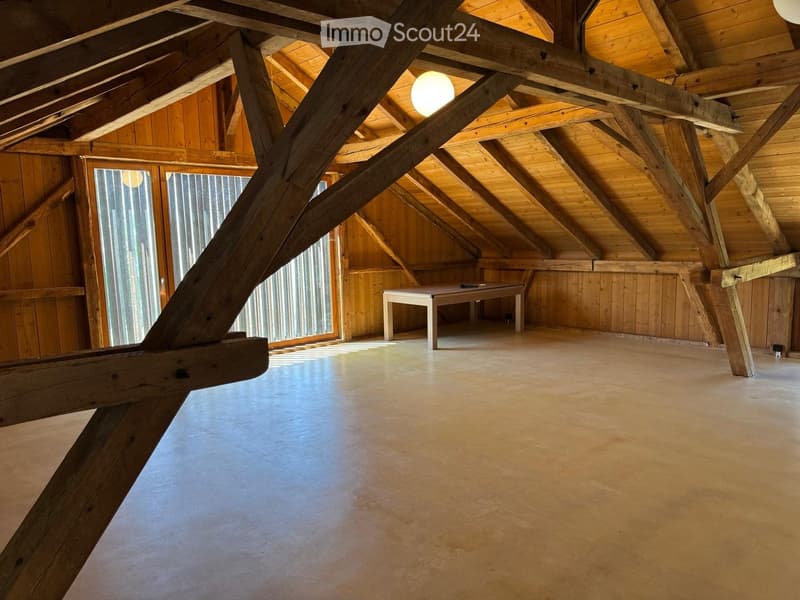 Loft-style room with exposed wooden beams, polished concrete floor, and a single table in the center.
