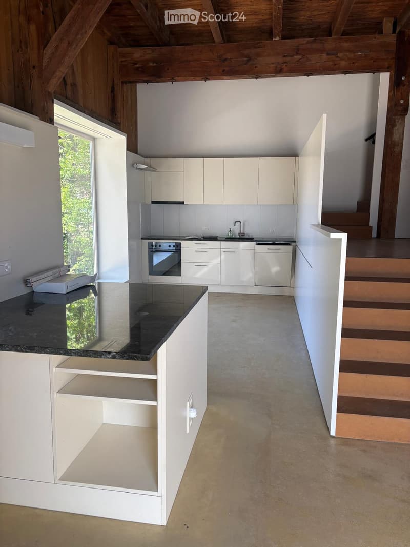 Modern kitchen with white cabinets, stainless steel appliances, and a black countertop. Features an island with open shelving and a staircase leading to an upper level.