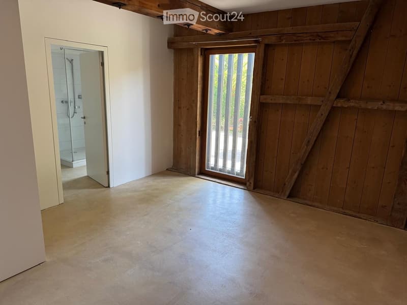 Empty room with wooden walls, concrete floor, and a large sliding glass door leading to an outdoor area. A shower stall is visible through an open doorway.