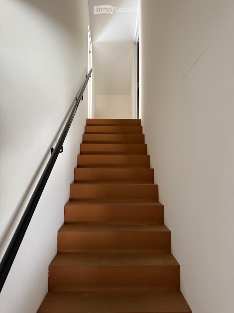Modern staircase with brown steps and a black metal handrail, set against white walls.