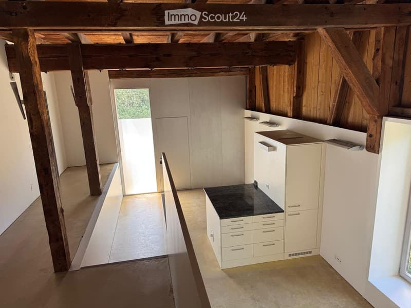 Modern kitchen with white cabinets, black countertop, and exposed wooden beams on the ceiling. The space is bright with natural light coming through a large window.