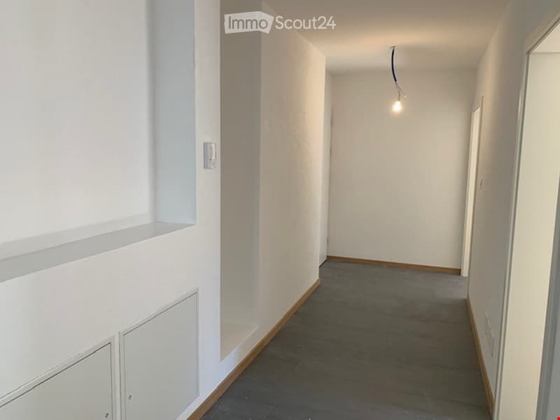 Empty hallway with white walls, grey tiled floor, and a single light fixture hanging from the ceiling.