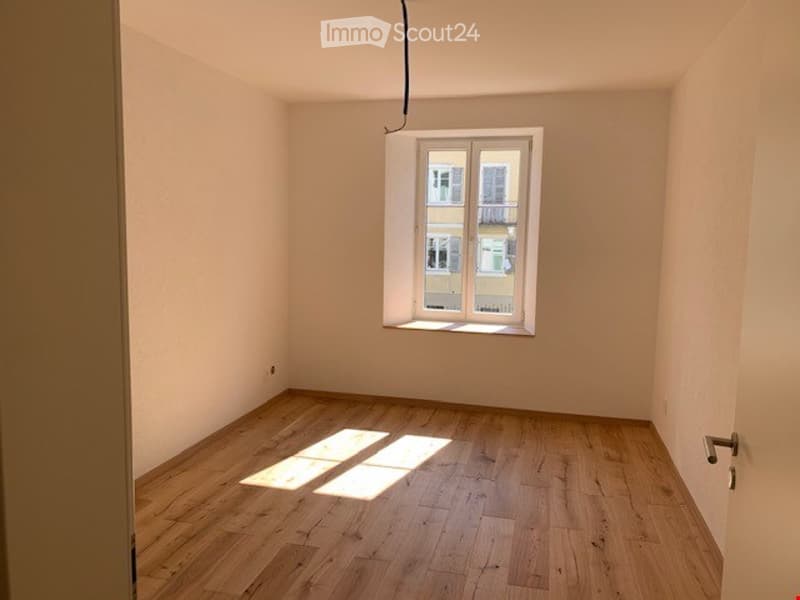 Empty room with wooden flooring and a single window letting in natural light. No furniture or equipment present.