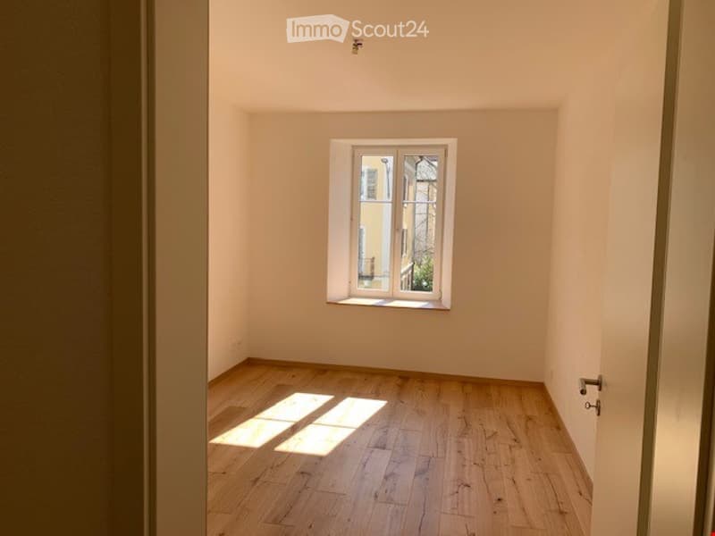 Empty room with wooden flooring and a single window letting in natural light. No furniture or equipment present.