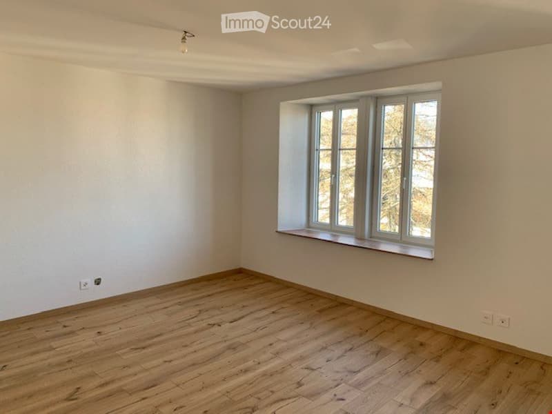 Empty room with wooden flooring, white walls, and a large window with multiple panes.