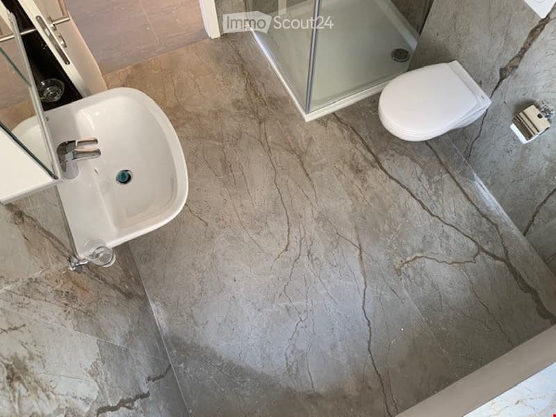 Modern bathroom with marble-effect flooring, white sink, toilet, and glass shower enclosure.