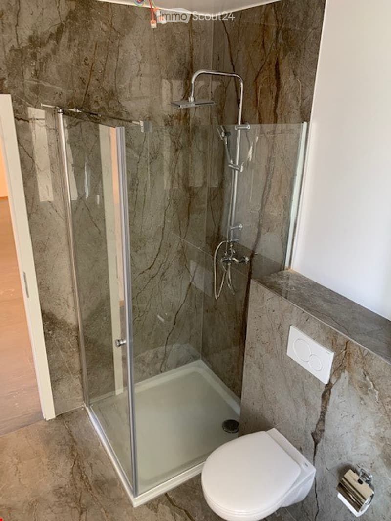 Modern bathroom with a glass-enclosed shower, toilet, and marble-style tiles.