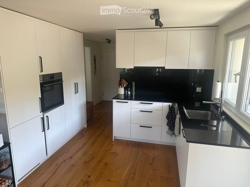 Modern kitchen with white cabinets, black countertops, and wooden flooring. Features an oven, sink, and various kitchen utensils.
