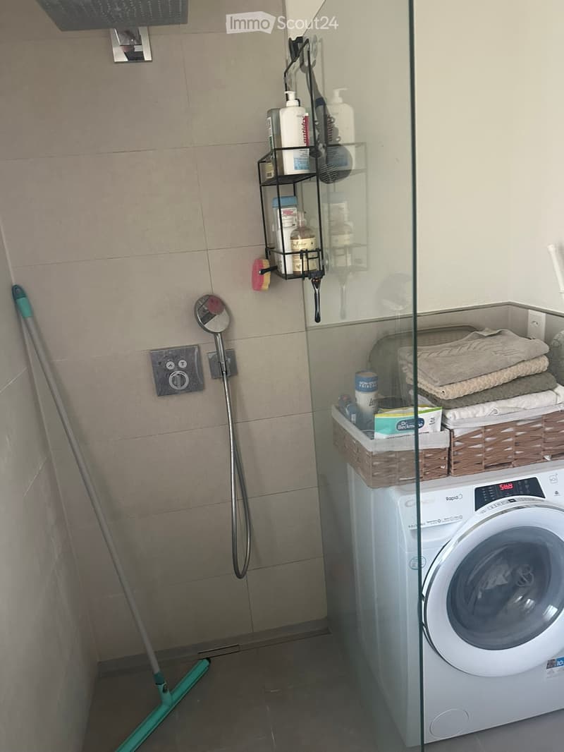 Bathroom with a washing machine, towels, shower, mirror, cleaning supplies, and shelves.