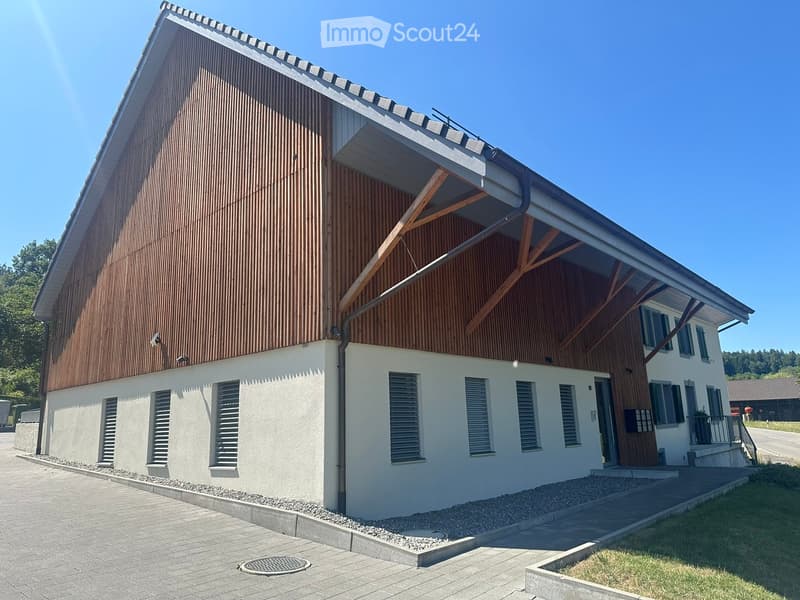 Modern two-story house with a combination of white and brown exterior walls, large windows, and a covered entrance area with wooden beams.