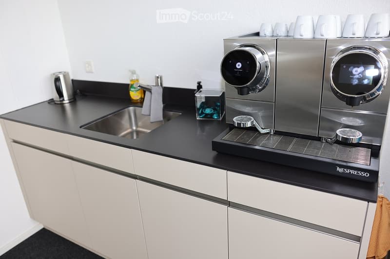 Modern kitchen with white cabinets, black countertop, stainless steel coffee machine, sink, and various small items.