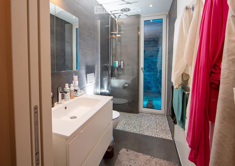 Modern bathroom with a white sink, chrome faucet, large mirror, toilet, glass-enclosed shower, and towels hanging on the wall.