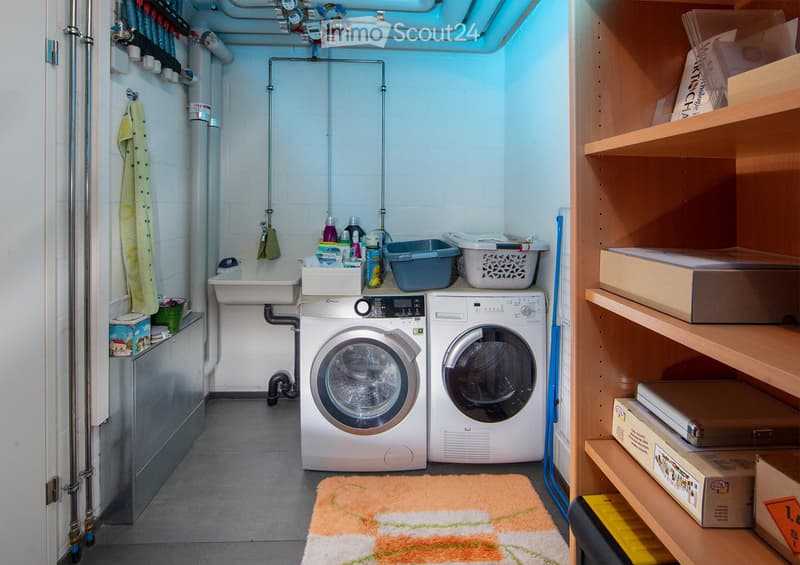Functional bathroom with a washing machine, dryer, sink, and shelves for storage. Includes a towel hanging on the wall and a small rug on the floor.