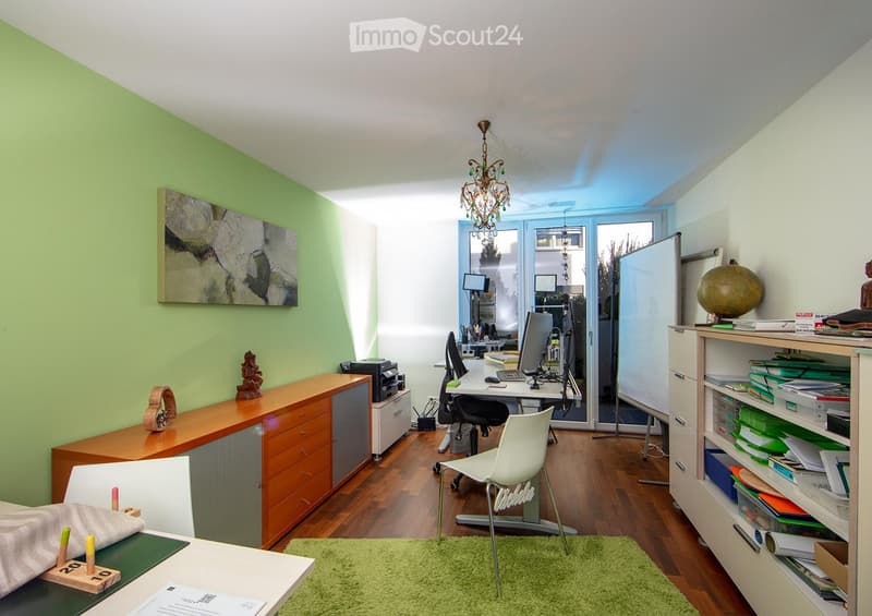 Office space with a wooden floor, green accent wall, white desk, laptop, chair, cabinet, shelf, globe, and artwork.
