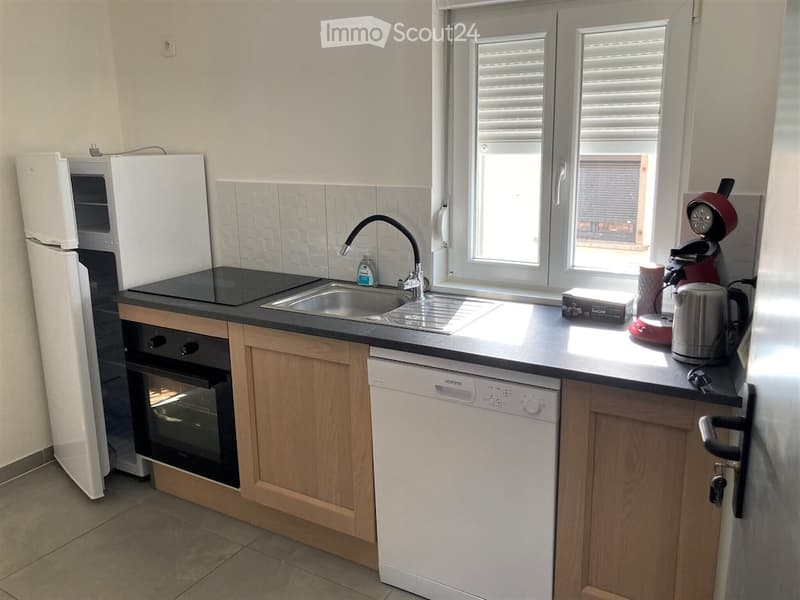 Modern kitchen with wooden cabinets, black countertops, stainless steel sink, and various appliances including a refrigerator, oven, dishwasher, coffee maker, and kettle.