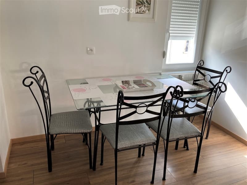 Dining area with a glass table, four black metal chairs with grey cushions, and a decorative table runner.