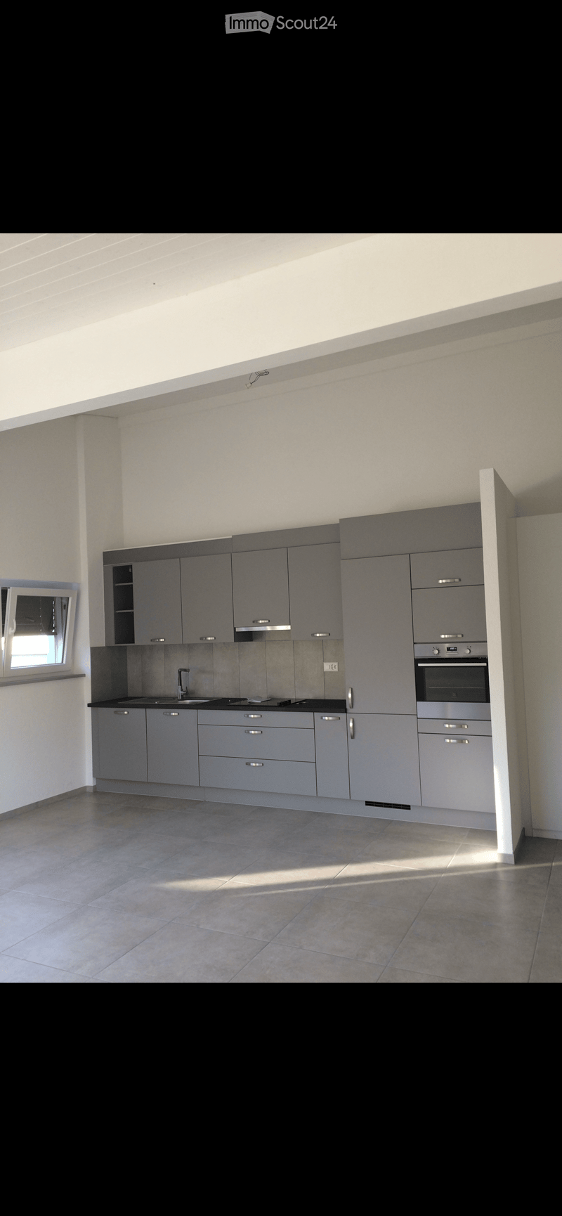 Modern kitchen with grey cabinets, stainless steel appliances, and a tiled floor. Features a sink, faucet, and oven.