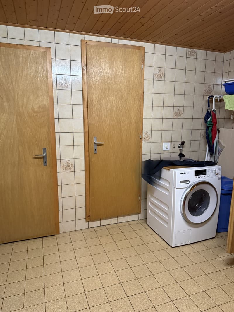 Small bathroom with tiled walls and floor, featuring a white washing machine, a faucet, and two wooden doors.